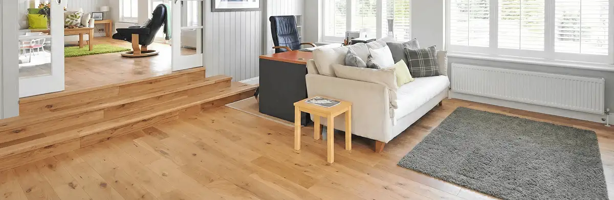 A modern living room with professionally installed laminate flooring, a beige sofa, a small side table, a gray rug, and large windows with white shutters in Portland, OR